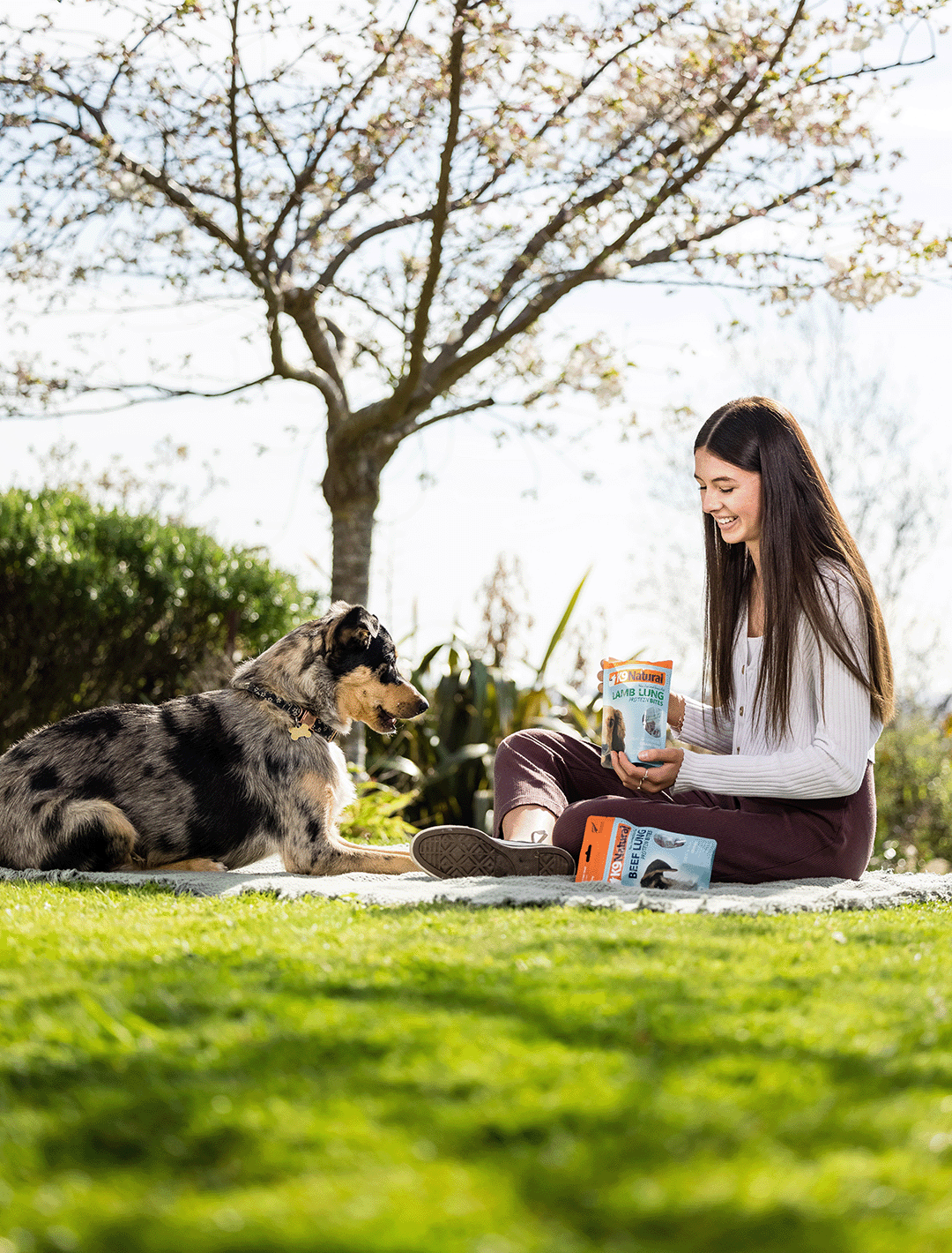 Girl Feeding mixed breed dog K9 Natural Lamb Lung Protein Bites on a picnic blanket